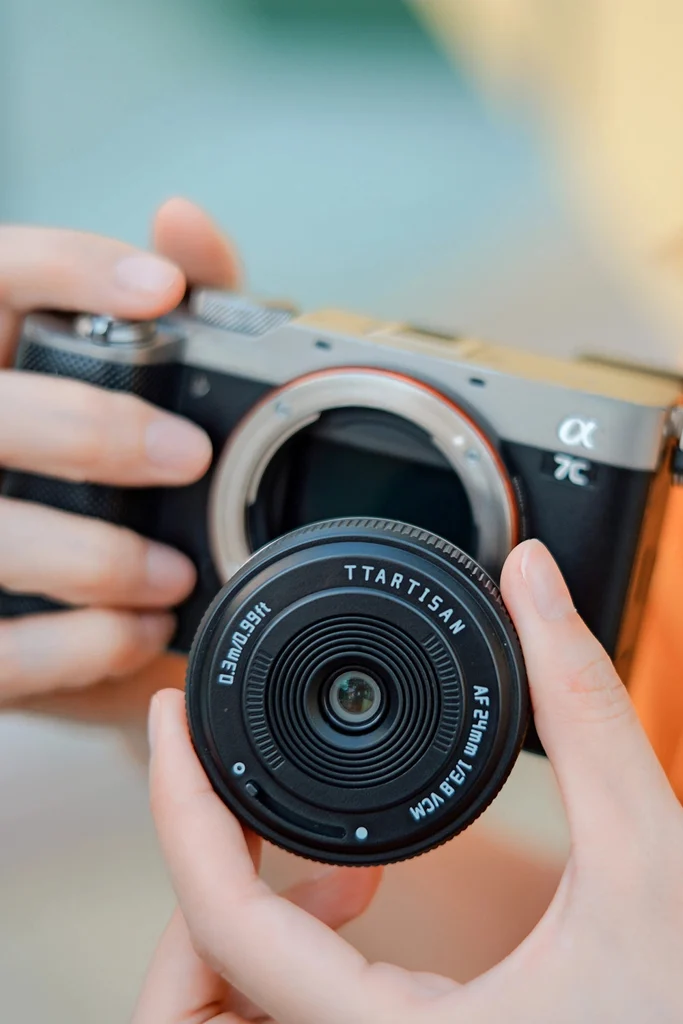 손에 든 TTArtisan AF 24mm F3.8 mini를 렌즈를 뺀 소니 α7C 바디 마운트 앞에 대어 본 모습